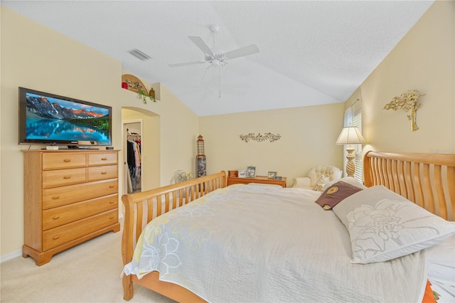 bedroom with light colored carpet, visible vents, a spacious closet, vaulted ceiling, and a textured ceiling