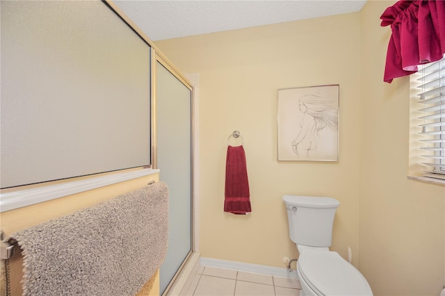 bathroom featuring toilet, a stall shower, a textured ceiling, tile patterned flooring, and baseboards