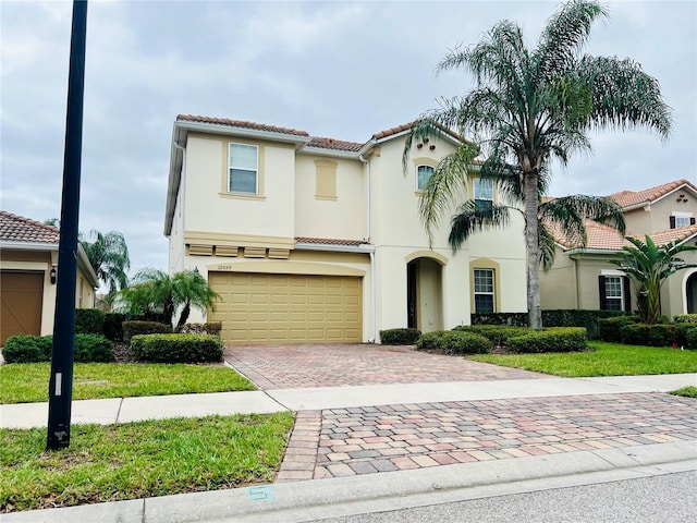 mediterranean / spanish-style home featuring a garage, stucco siding, decorative driveway, and a tiled roof