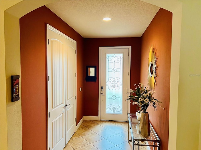 entryway with arched walkways, a textured ceiling, light tile patterned flooring, and baseboards