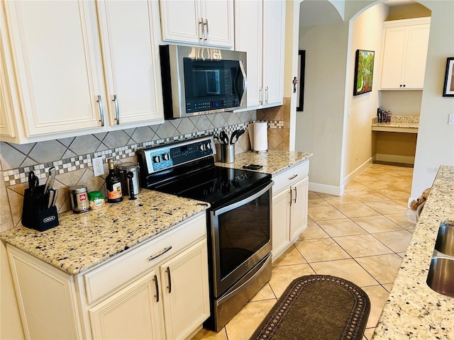 kitchen with arched walkways, light tile patterned floors, tasteful backsplash, appliances with stainless steel finishes, and baseboards