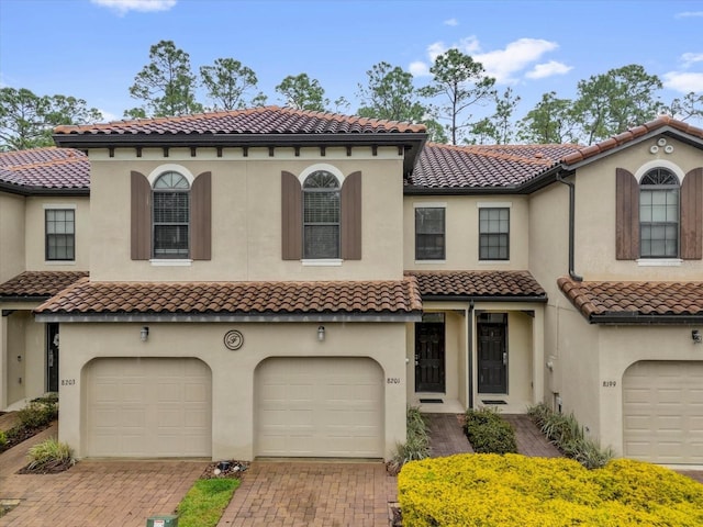 mediterranean / spanish-style house featuring an attached garage, decorative driveway, and stucco siding