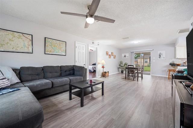 living area with a textured ceiling, ceiling fan, baseboards, and light wood-style floors