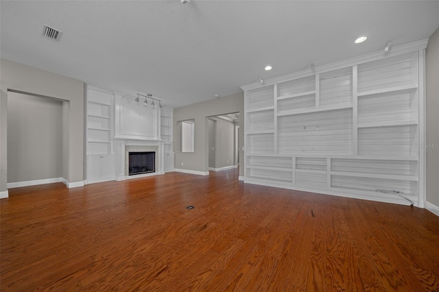 unfurnished living room with baseboards, visible vents, wood finished floors, built in shelves, and a fireplace