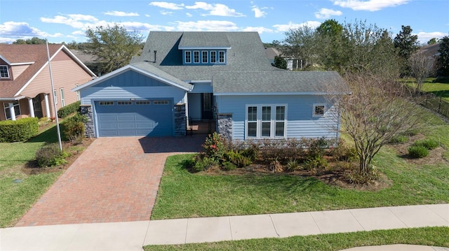 view of front facade with decorative driveway, a shingled roof, an attached garage, a front yard, and stone siding