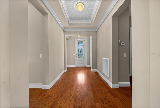 foyer featuring wood finished floors, visible vents, baseboards, a tray ceiling, and crown molding