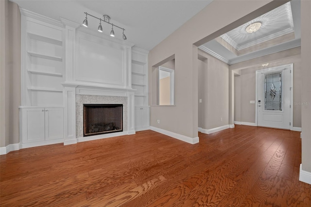 unfurnished living room with built in shelves, a fireplace, baseboards, and wood finished floors