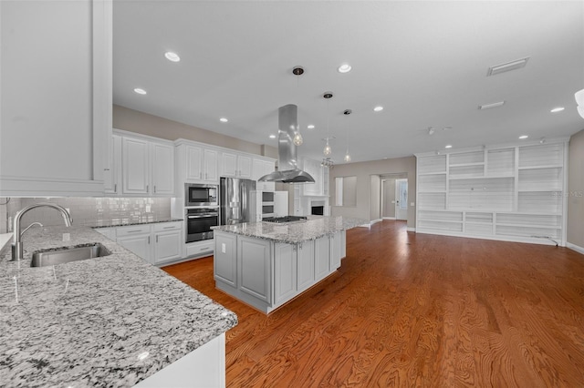 kitchen with island exhaust hood, appliances with stainless steel finishes, white cabinets, a sink, and a kitchen island