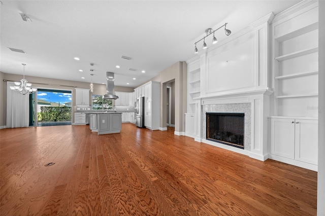 unfurnished living room featuring baseboards, built in features, wood finished floors, a fireplace, and a notable chandelier