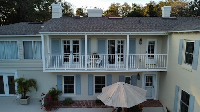 rear view of property featuring a shingled roof, a chimney, a balcony, and stucco siding