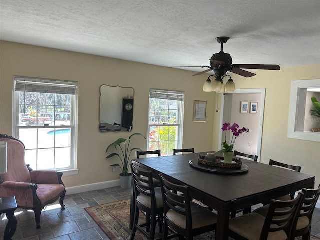 dining space with stone tile flooring, ceiling fan, a textured ceiling, and baseboards