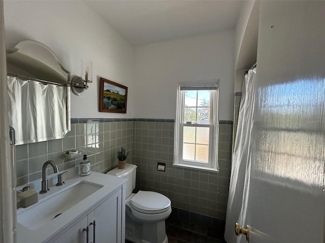 full bathroom featuring toilet, wainscoting, tile walls, and vanity