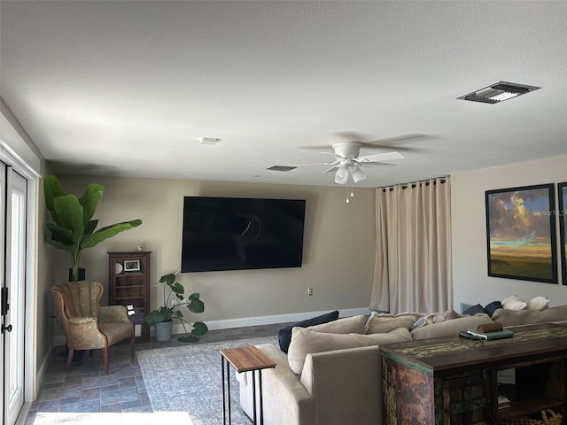 living room featuring a textured ceiling, a ceiling fan, visible vents, baseboards, and stone finish floor