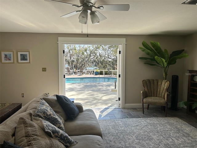 living room with ceiling fan, a textured ceiling, stone tile flooring, and baseboards