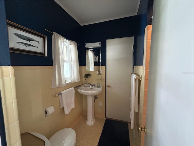 half bath with toilet, wainscoting, a sink, and tile walls