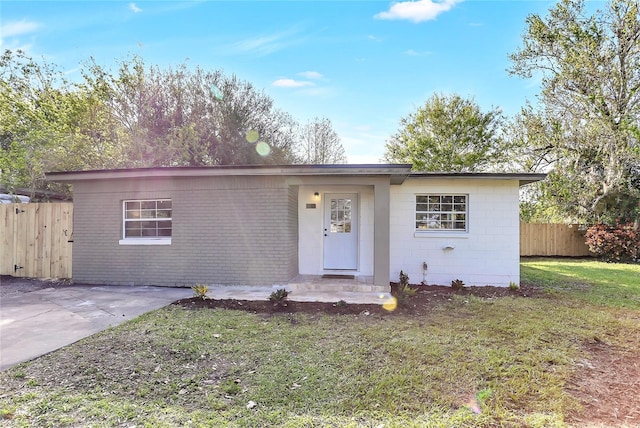 ranch-style home featuring a front yard, concrete block siding, fence, and driveway