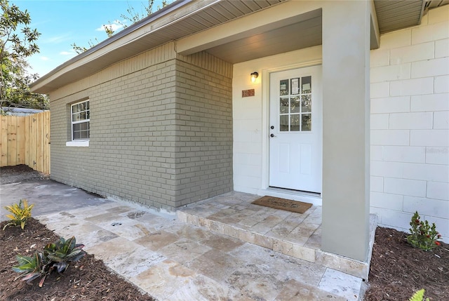 view of exterior entry with a patio area, fence, and brick siding