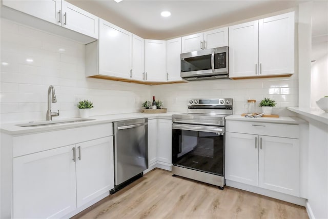 kitchen featuring light wood finished floors, white cabinets, stainless steel appliances, light countertops, and a sink