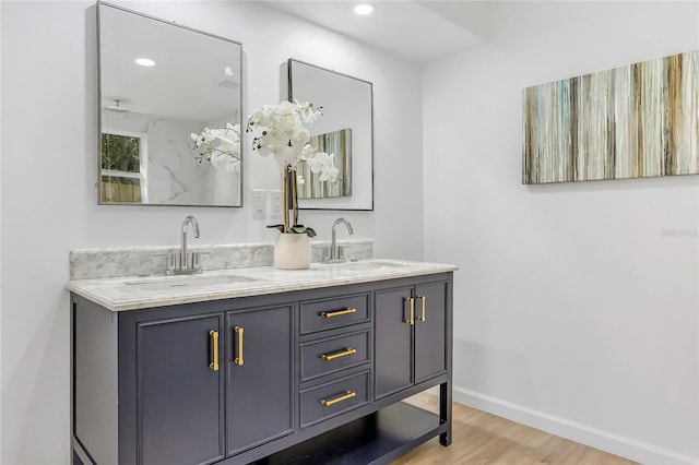 bathroom with double vanity, baseboards, a sink, and wood finished floors