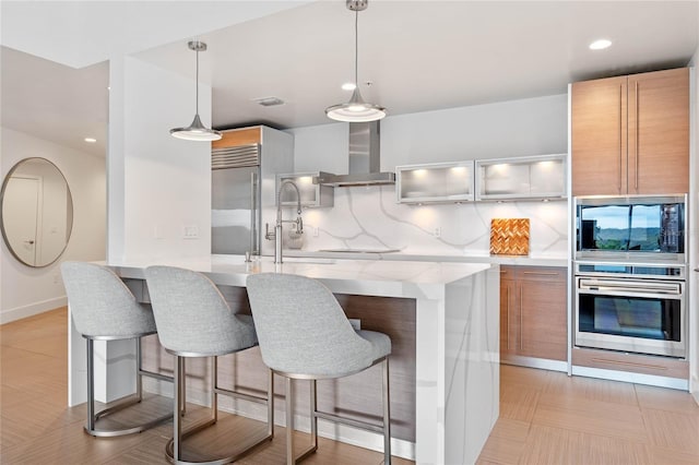 kitchen with built in appliances, wall chimney range hood, a breakfast bar, and tasteful backsplash