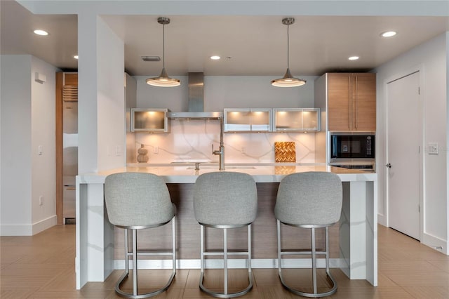 kitchen with black microwave, a breakfast bar area, light countertops, wall chimney range hood, and tasteful backsplash