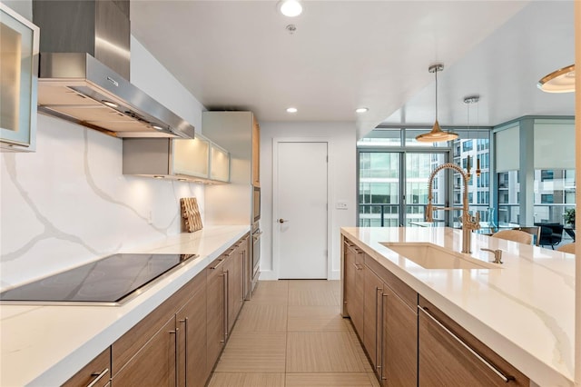 kitchen with decorative backsplash, brown cabinetry, a sink, wall chimney range hood, and black electric cooktop