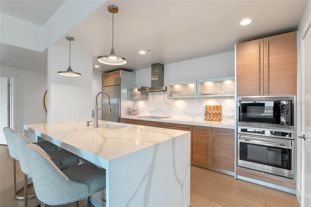 kitchen with built in appliances, a sink, brown cabinets, wall chimney exhaust hood, and tasteful backsplash