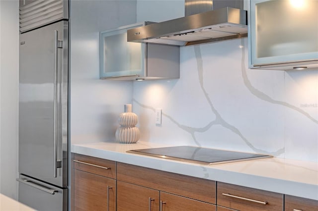 kitchen featuring brown cabinets, light countertops, stainless steel built in fridge, and wall chimney exhaust hood