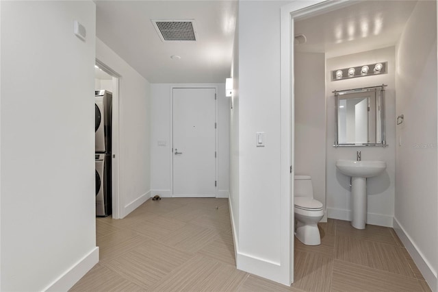 half bath with stacked washer and clothes dryer, visible vents, toilet, baseboards, and tile patterned floors