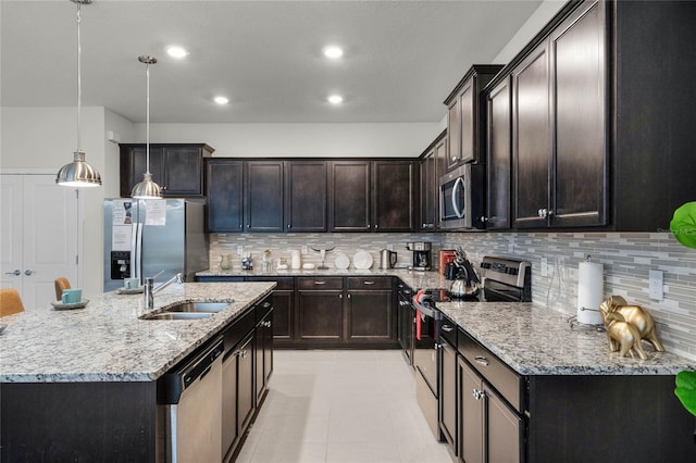 kitchen featuring light stone counters, pendant lighting, a center island with sink, stainless steel appliances, and dark brown cabinets