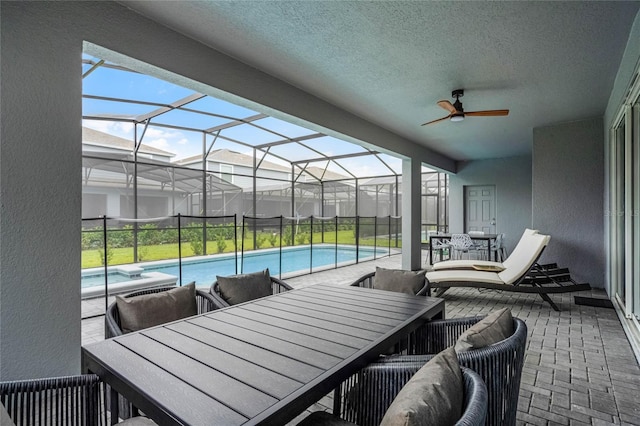 view of patio / terrace featuring glass enclosure, a pool with connected hot tub, a ceiling fan, and outdoor dining space