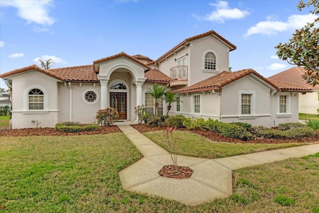 mediterranean / spanish-style home with a front lawn, a tile roof, a balcony, and stucco siding