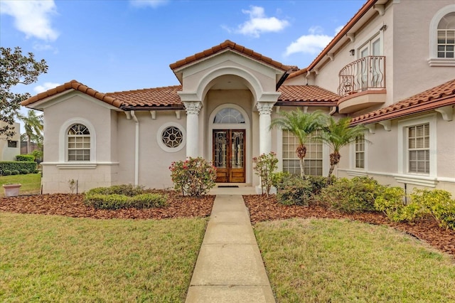 view of exterior entry with a yard, a balcony, and stucco siding