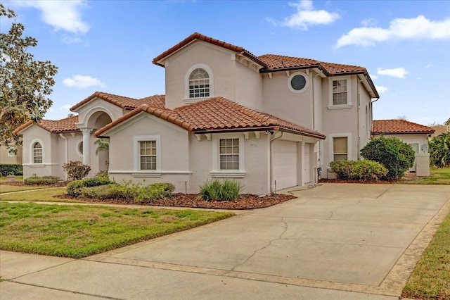 mediterranean / spanish house featuring driveway, a garage, a tiled roof, a front yard, and stucco siding