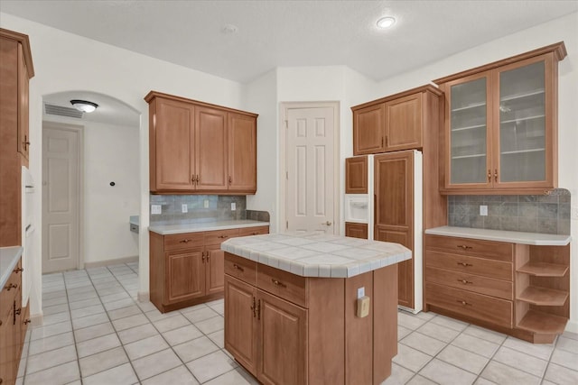 10616 Emerald Chase Dr, Orlando, FL 32836 - kitchen with arched walkways, tile countertops, a kitchen island, glass insert cabinets, and light tile patterned flooring