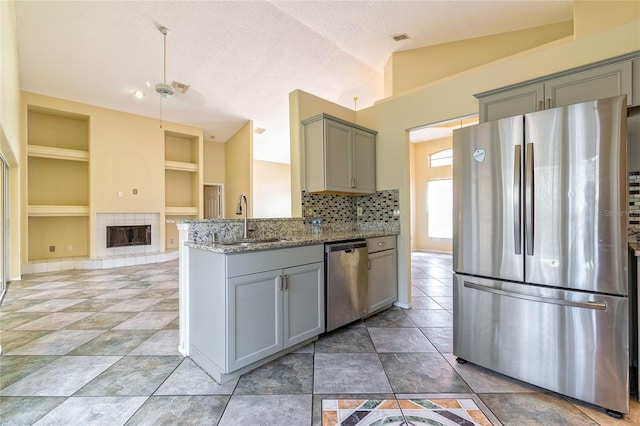 kitchen with light stone counters, a tile fireplace, a sink, vaulted ceiling, and appliances with stainless steel finishes