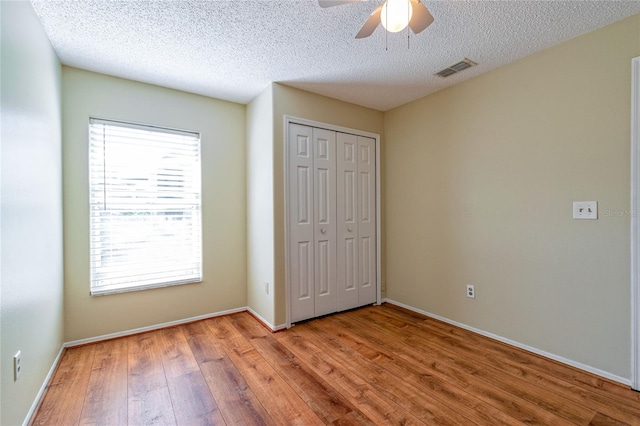 unfurnished bedroom with a textured ceiling, light wood finished floors, a closet, and baseboards