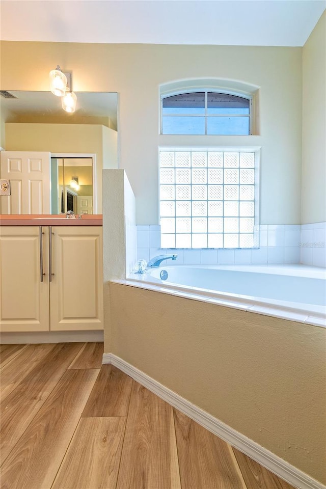 full bath featuring vanity, visible vents, a bath, and wood finished floors