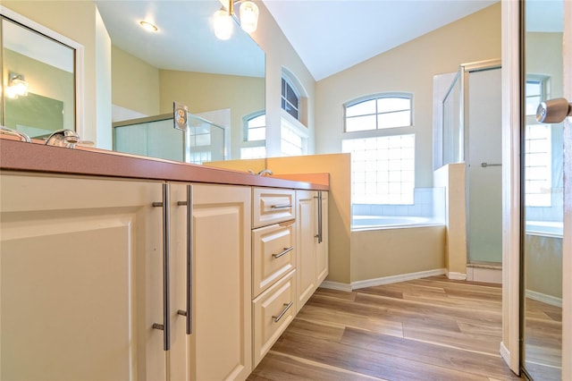 full bath with a stall shower, lofted ceiling, wood finished floors, vanity, and a bath