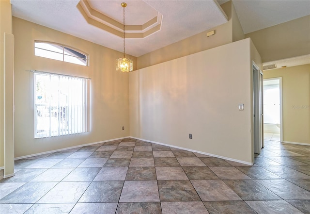 spare room with a notable chandelier, a tray ceiling, visible vents, and baseboards