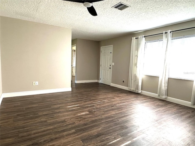 spare room featuring dark wood-style floors, visible vents, a ceiling fan, a textured ceiling, and baseboards