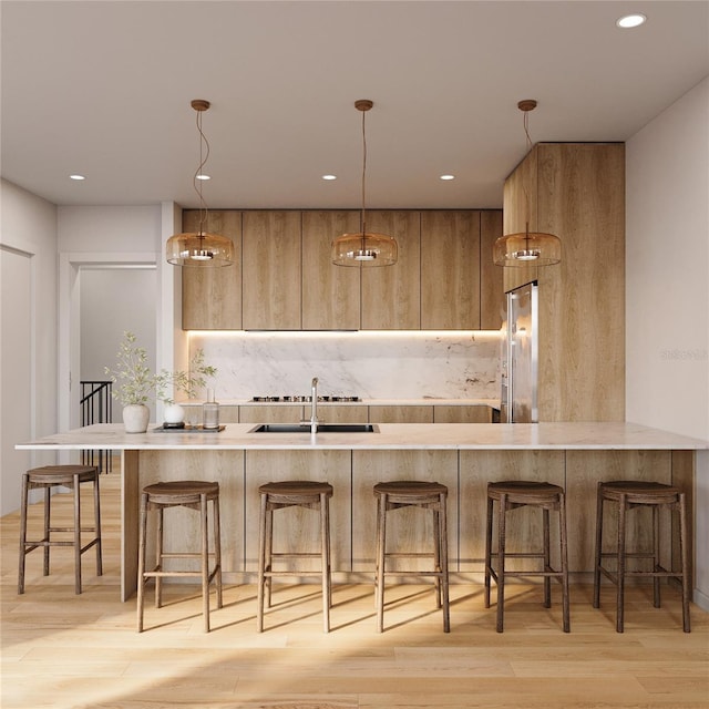 kitchen featuring pendant lighting, light countertops, light wood-style flooring, high quality fridge, and a sink