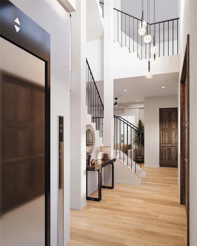 entryway with a towering ceiling, elevator, ceiling fan, light wood-type flooring, and stairs