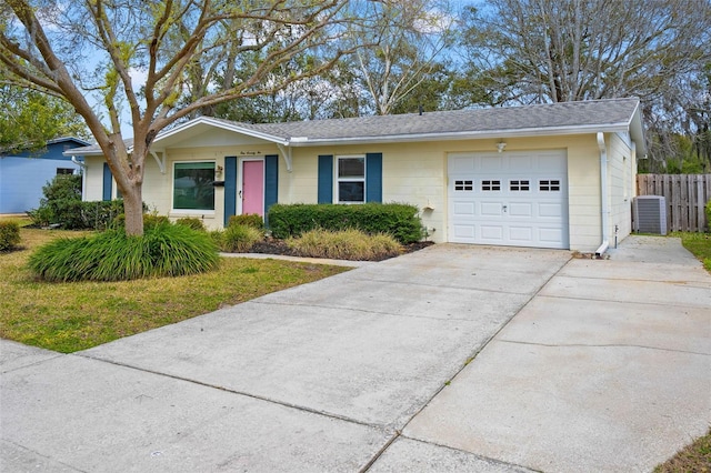 single story home featuring a garage, driveway, a shingled roof, central AC unit, and fence