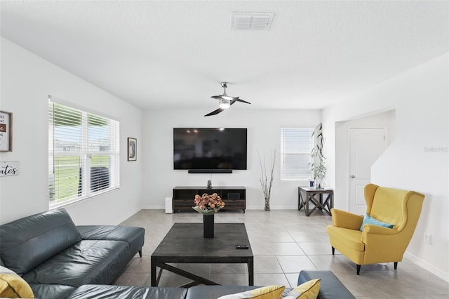 living area with light tile patterned floors, ceiling fan, visible vents, and baseboards