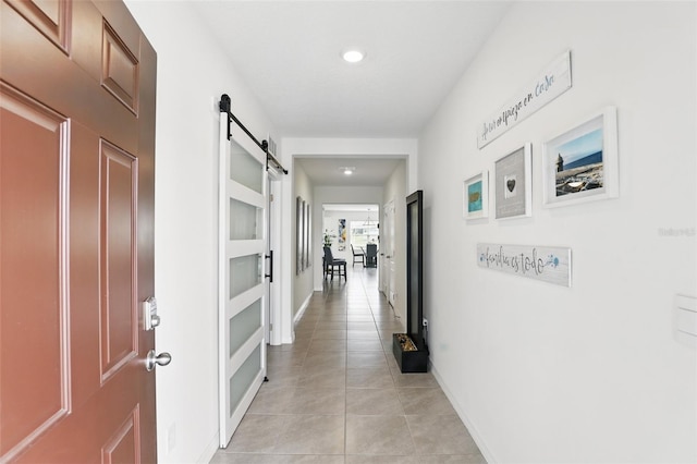 hall featuring a barn door, baseboards, and light tile patterned flooring