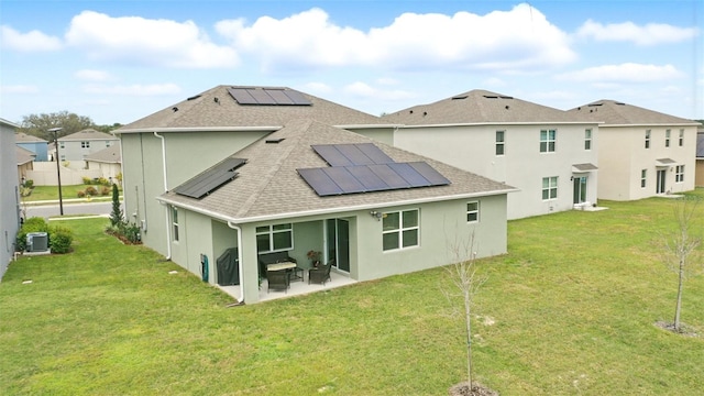 rear view of house with a patio, solar panels, roof with shingles, a lawn, and stucco siding