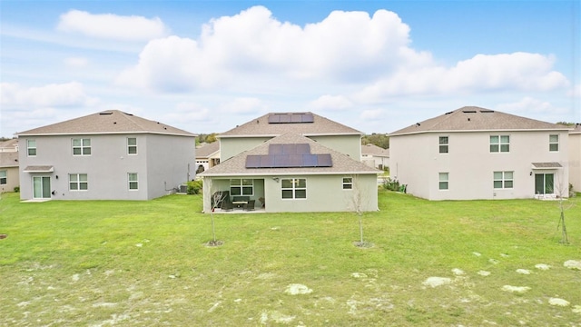 rear view of property with a patio, a lawn, and roof mounted solar panels