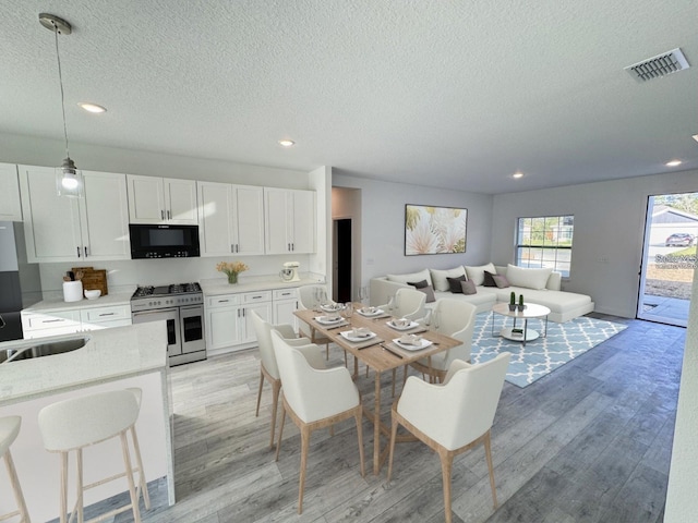 dining room featuring light wood-style floors, recessed lighting, visible vents, and a textured ceiling