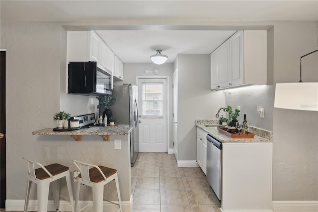 kitchen featuring a breakfast bar area, light tile patterned floors, appliances with stainless steel finishes, white cabinets, and a sink